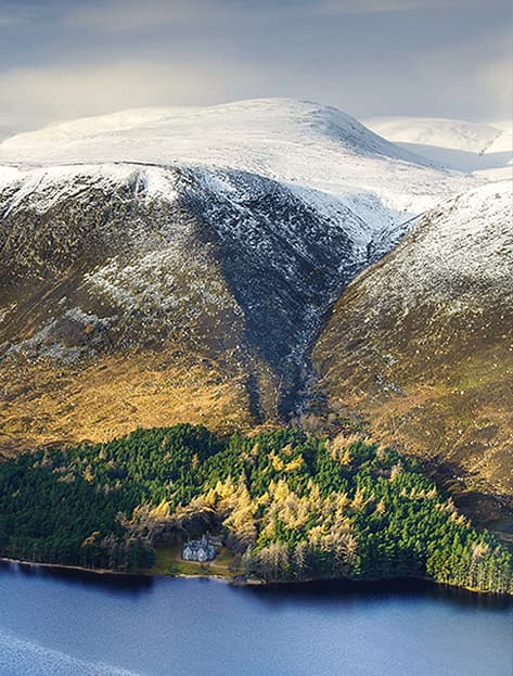 Snow dusted mountains above forested lake in Balmoral, Scotland